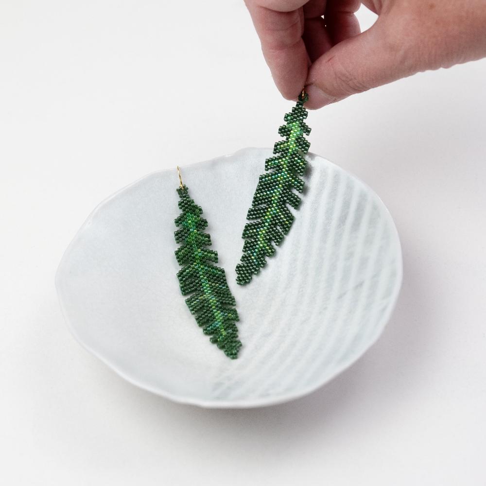 Banana Leaf Earrings on a ceramic bowl with a hand model.