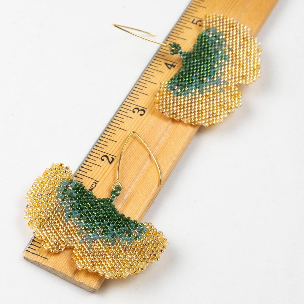 Golden ginkgo earrings of glass beads with wooden ruler in inches.