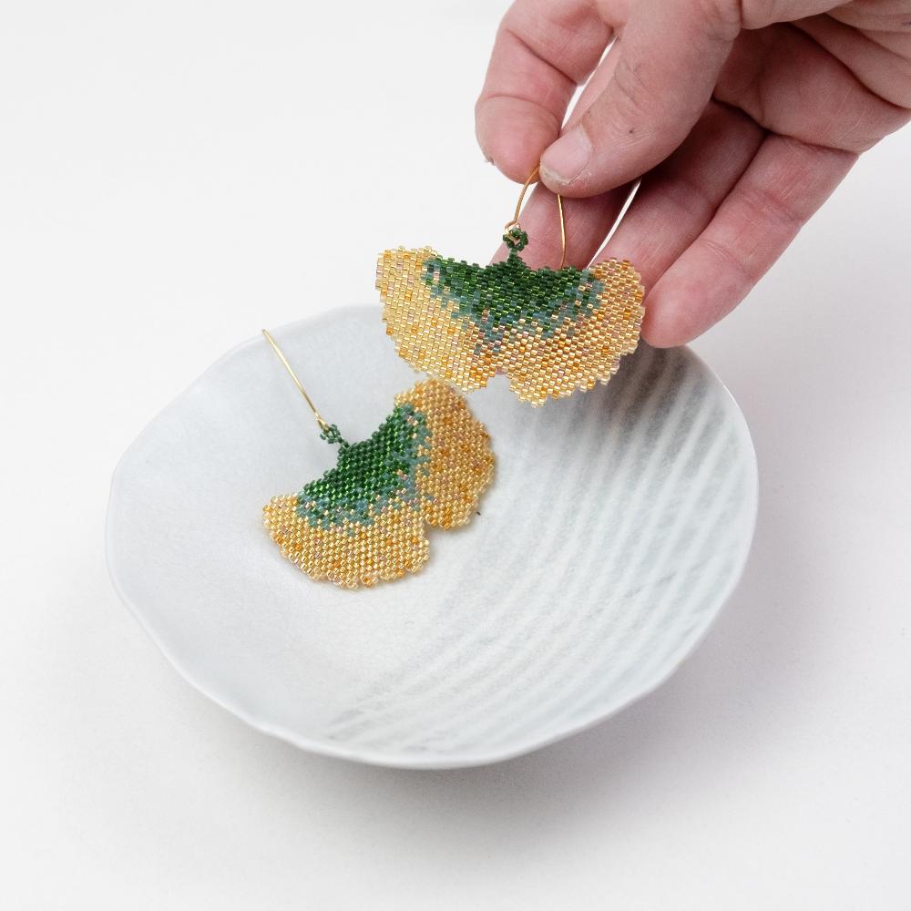 Golden ginkgo earrings of glass beads with a hand model