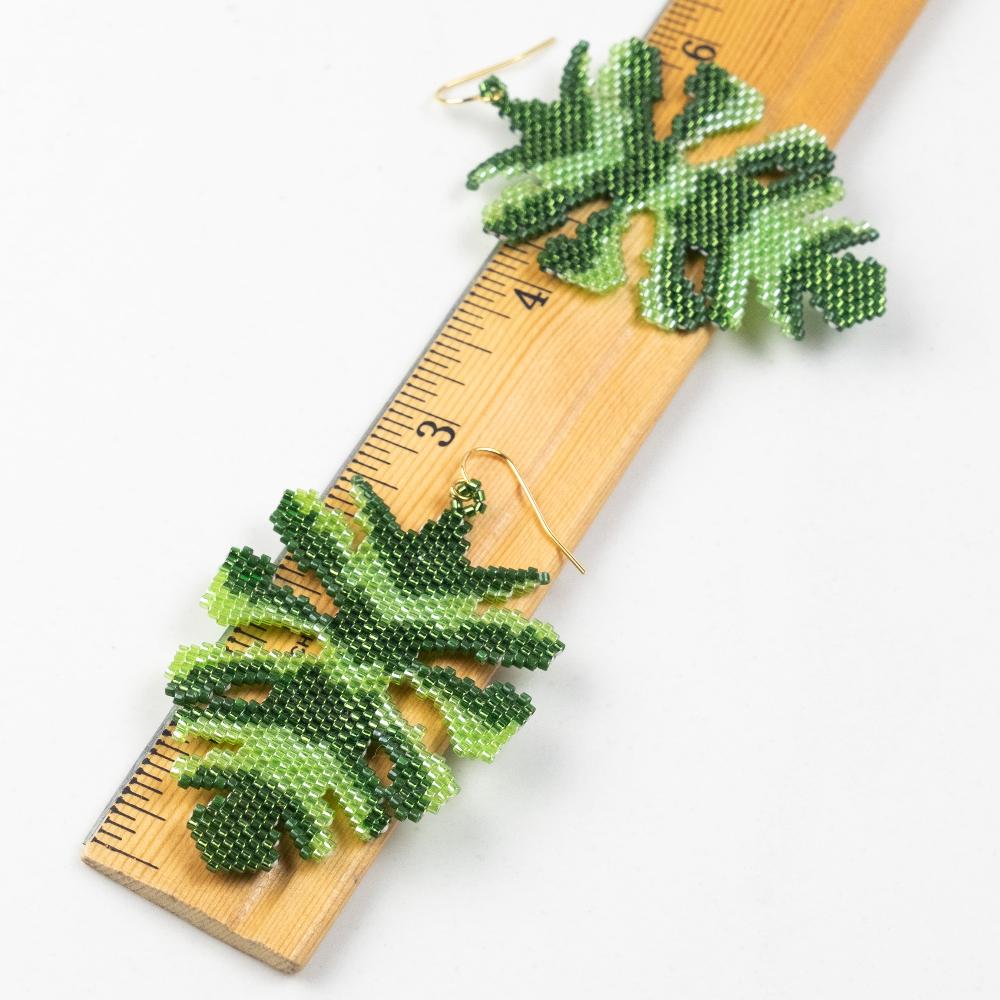 Monstera leaf earrings made of glass beads with a wooden ruler.