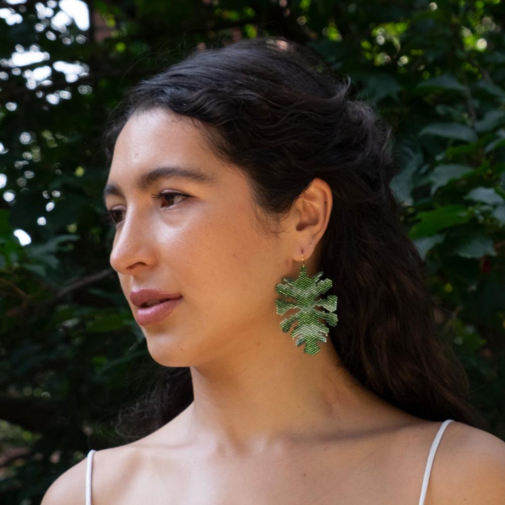 Colombian model wearing monstera leaf earrings made of glass beads.